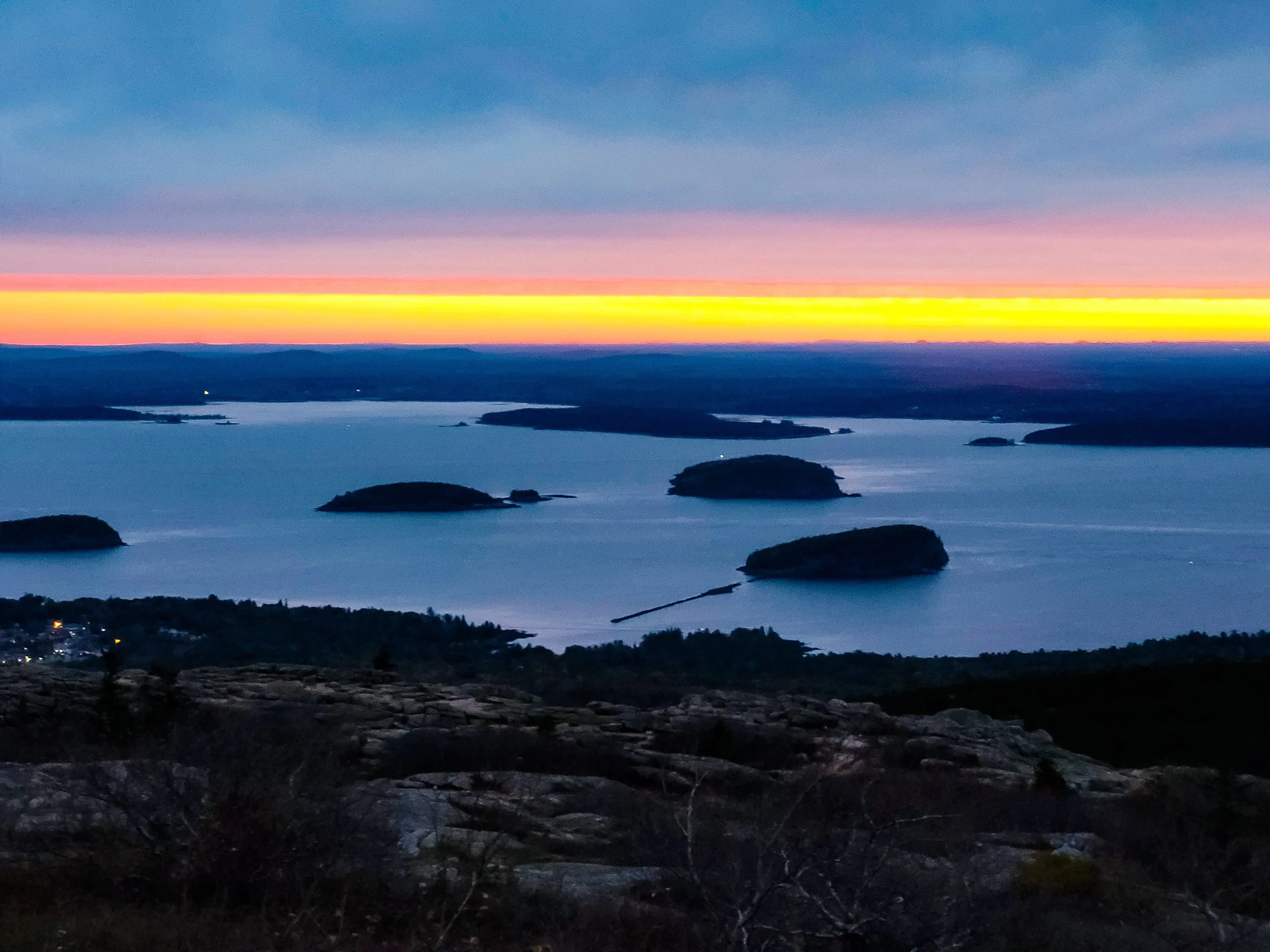Sunrise from the summit of Cadillac Mountain, low light across bare granite and the islands of Frenchman Bay below